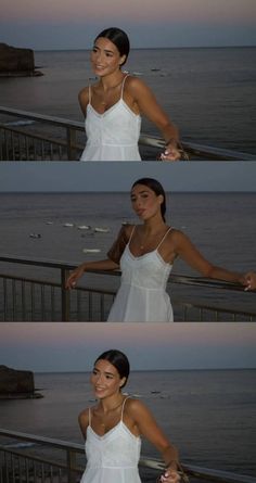 a woman in white dress standing next to the ocean at sunset with her arms outstretched