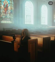 a woman sitting in the pews of a church with stained glass windows behind her