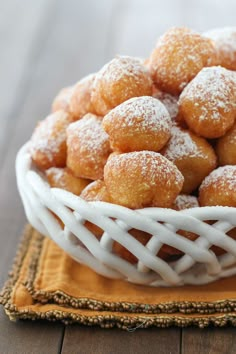 powdered sugar covered donuts in a white bowl on a yellow napkin and wooden table