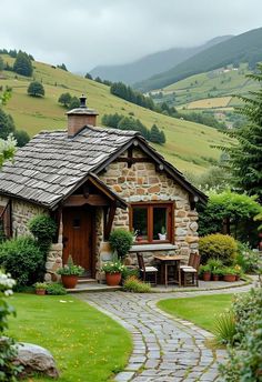 a small stone house in the middle of a lush green field with mountains behind it