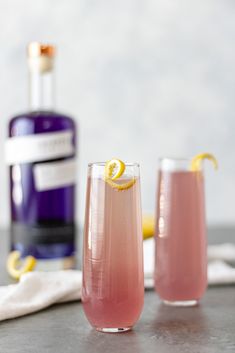 two glasses filled with pink lemonade next to a bottle