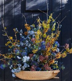 a basket filled with lots of flowers sitting on top of a wooden table next to a wall