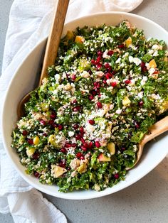 a white bowl filled with lots of food on top of a table next to a wooden spoon