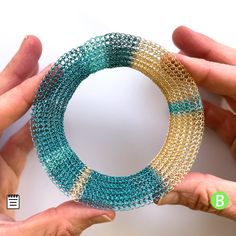 two hands are holding a bracelet made out of chain mail and plastic beads with the letter b on it