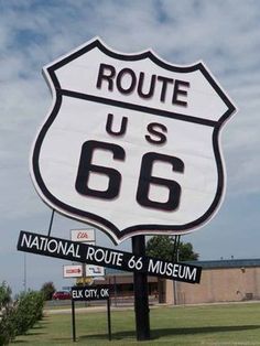 a large sign for route 66 in the middle of a grassy area next to a building