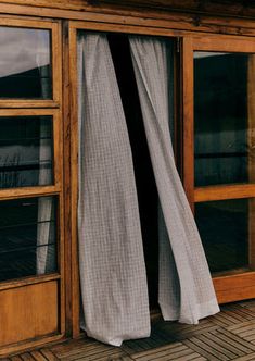 an open window on the outside of a wooden building with curtains hanging from it's sides