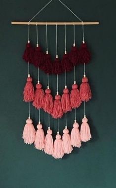 the pink and red tassels are hanging from a wooden hanger on a green wall