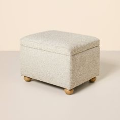 an upholstered foot stool with wooden legs and a light colored fabric cover on top