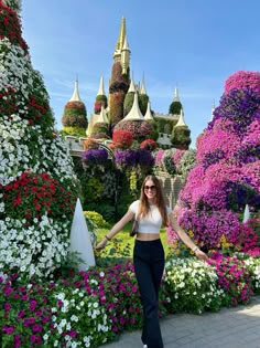 a woman is standing in front of flowers and trees with her arms spread out to the side