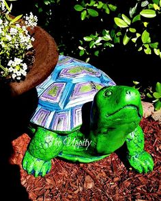 a green turtle statue sitting on top of mulch next to a potted plant