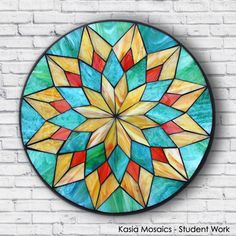 a circular stained glass window hanging on a brick wall with the words kalei mosaics student work