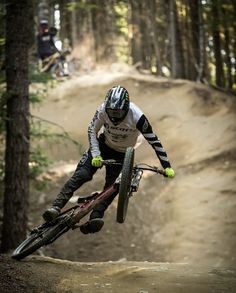 a man riding a bike on top of a dirt trail in the woods with trees