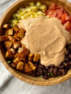 a wooden bowl filled with beans, tofu, corn, and other food items