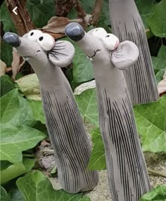 two clay mice are standing on their hind legs in front of green leaves and plants