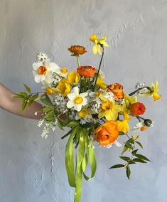 a person holding a bouquet of flowers in front of a gray wall with white and yellow flowers