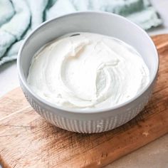 a white bowl filled with whipped cream sitting on top of a wooden cutting board next to a blue towel