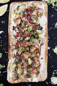 a flat bread with vegetables on it next to lemon wedges and other toppings