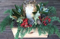 a candle and some pine cones are on a wooden box with greenery, berries and candlesticks