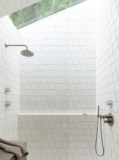 a white tiled bathroom with a skylight above the tub and shower head on the wall