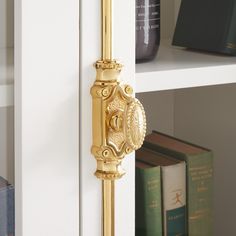 a gold door handle on the side of a white bookcase with books behind it