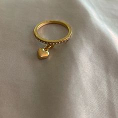 a gold ring with a heart on it sitting on top of a white cloth covered surface