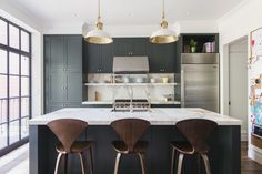 three stools sit in front of an island with marble countertops and stainless steel appliances