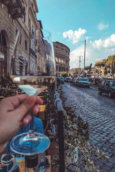 a person holding a glass of wine in front of a street lined with parked cars