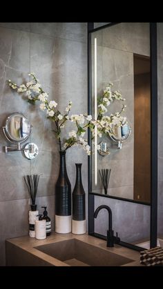 a bathroom sink sitting under a large mirror next to a vase with flowers in it