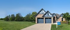 a house with two garages and a blue sign in front of it on the grass