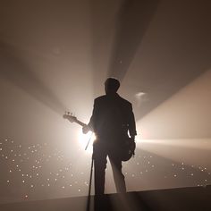 a man with a guitar standing in front of a spotlight filled stage while the sun shines down on him