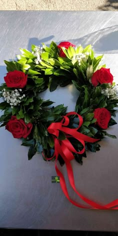 a wreath with red roses and greenery on it sitting on a white table cloth