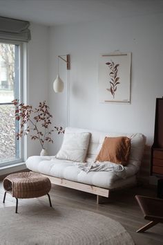 A small living room with transformable sofa bed with pine wood frame and beige futon mattress. Room is decorated with a small plant in a vase, a botanical poster on the wall and organic lamp hanging from the wall. Sofa is decorated with 3 cushions and a clay brown plaid. In one of the images there is a hairy, cute cat sleeping with his for paws in the air. Office With Sofa Bed, Home Office With Sofa, Sofa Bed Guest Room, Timeless Sofa, Sofa Bed Design, Sofa Cama, Futon Sofa Bed, Futon Bed, Office Sofa