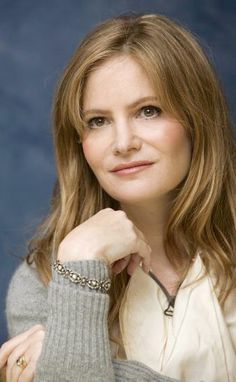 a woman with long hair wearing a sweater and bracelet posing for a photo in front of a blue background