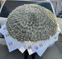 a person standing next to a white car with money on it's hood and an umbrella made out of rolled up dollar bills