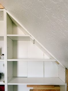 a room with white shelves and cabinets under the roof, in front of a window