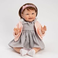 a baby doll sitting on the ground with her hands in the air and wearing a gray dress