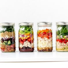 four mason jars filled with different types of salads and vegetables, all lined up in the same row