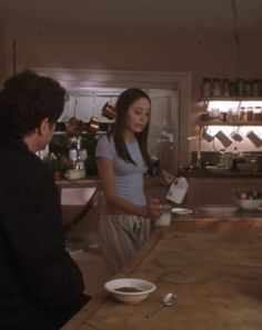 two people standing at a counter in a kitchen, one person pouring something into a bowl