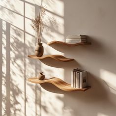 three wooden shelves with books and vases on them against a wall in the sunlight