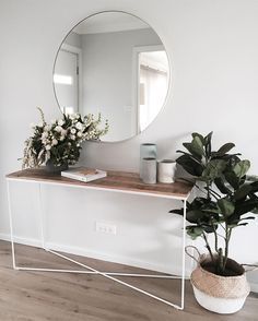 there is a mirror and some plants on the counter in this room with white walls