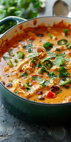 a green pot filled with soup and garnished with cilantro, red pepper, and other vegetables