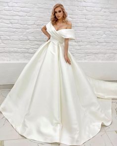 a woman in a white wedding dress standing on the floor next to a brick wall