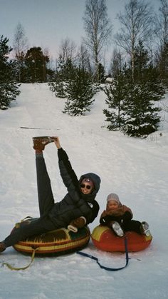 two people laying in the snow on sleds