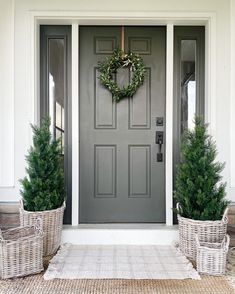 the front door is decorated with wreaths and potted plants on either side, along with two wicker baskets