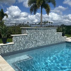 an empty swimming pool with blue water and palm trees in the background