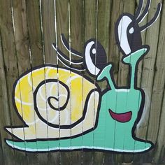 a painting on the side of a wooden fence depicting a snail with yellow and black stripes