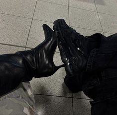 a pair of black boots sitting on top of a tiled floor next to a person's leg