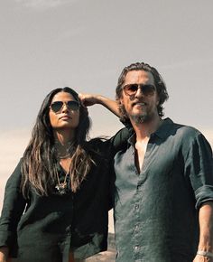 a man and woman standing next to each other in front of the desert with mountains behind them