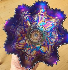 a hand holding a purple glass bowl with an intricate design on it's center