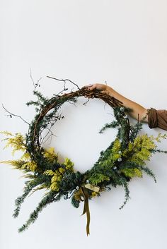 a hand holding a wreath with green and yellow flowers